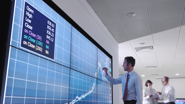 man at video wall looking at stock prices